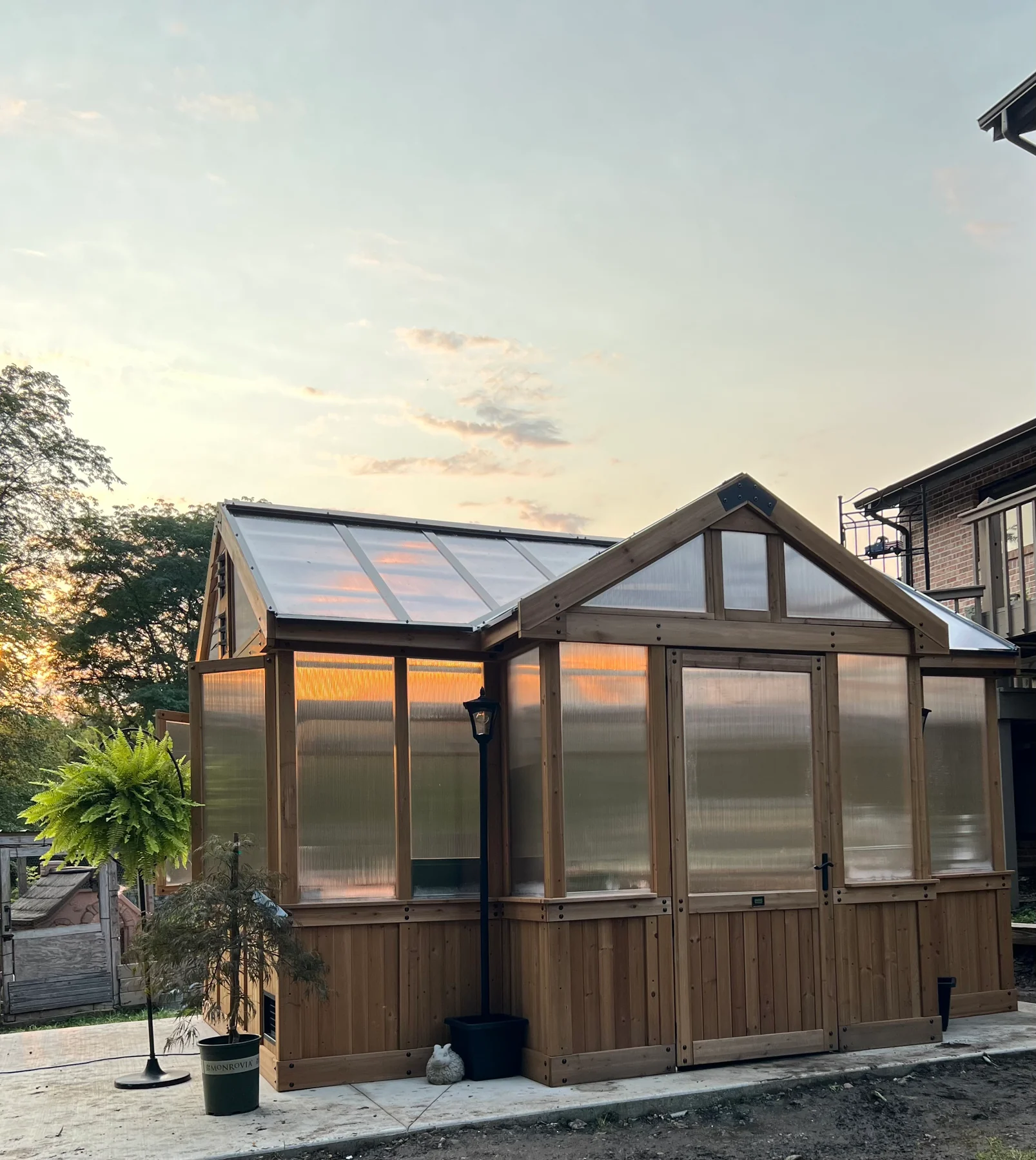 After assembly: the wooden greenhouse with its framed walls, light-transmitting panels, and roof visible in the evening light.