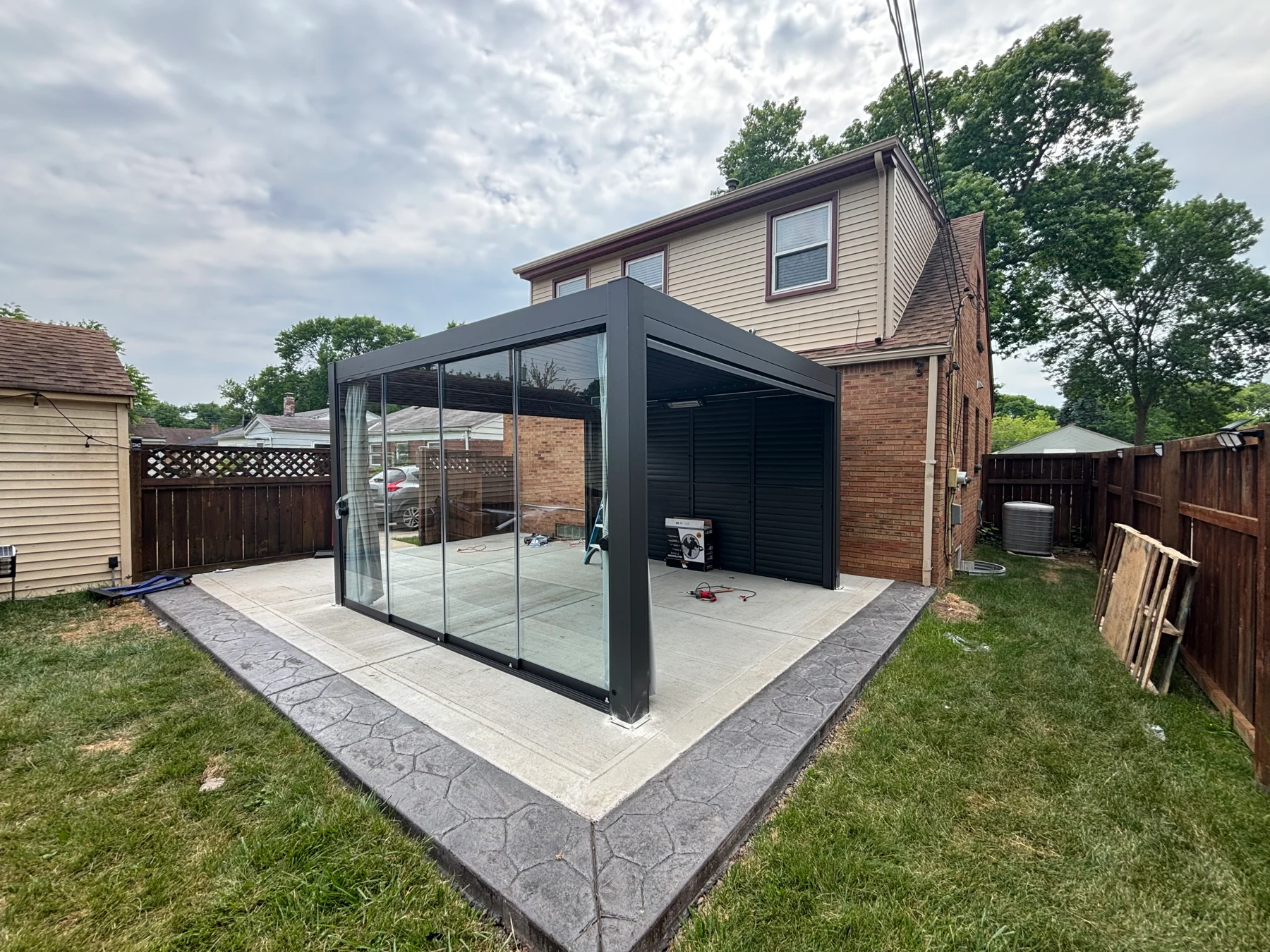 After assembly: an angled view showing the glass frontage, roof, and shaded side of the pergola on the patio.