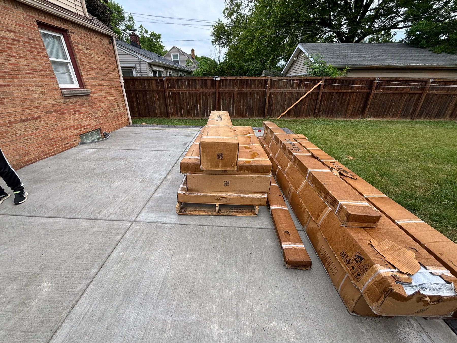 Before assembly: the packaged pergola components stacked on the patio beside the house.